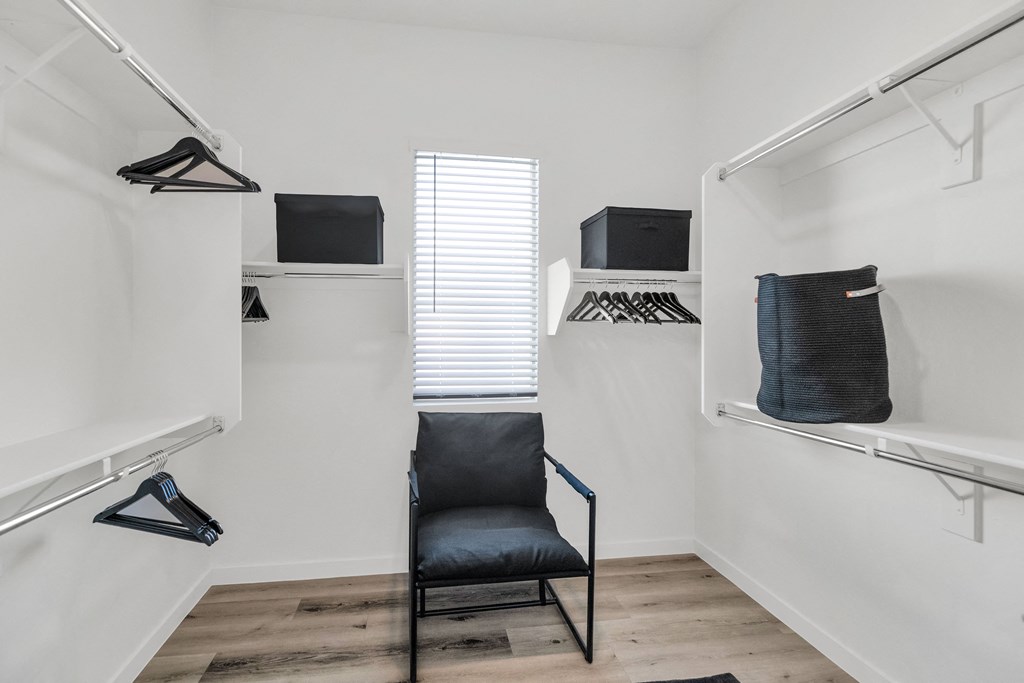 A black chair is in the middle of a white room with clothes hanging on a rail.at Marketside Villas at Verrado, Arizona, 85396