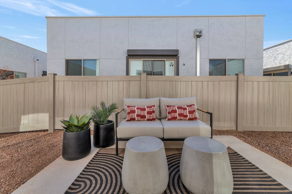 A modern outdoor living space with a white couch, two black planters, and a striped rug.at Marketside Villas at Verrado, Buckeye, AZ