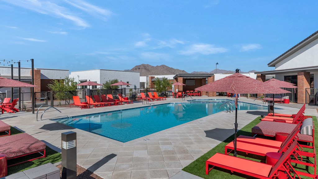 A pool surrounded by red chairs and umbrellas.at Marketside Villas at Verrado, Buckeye, 85396