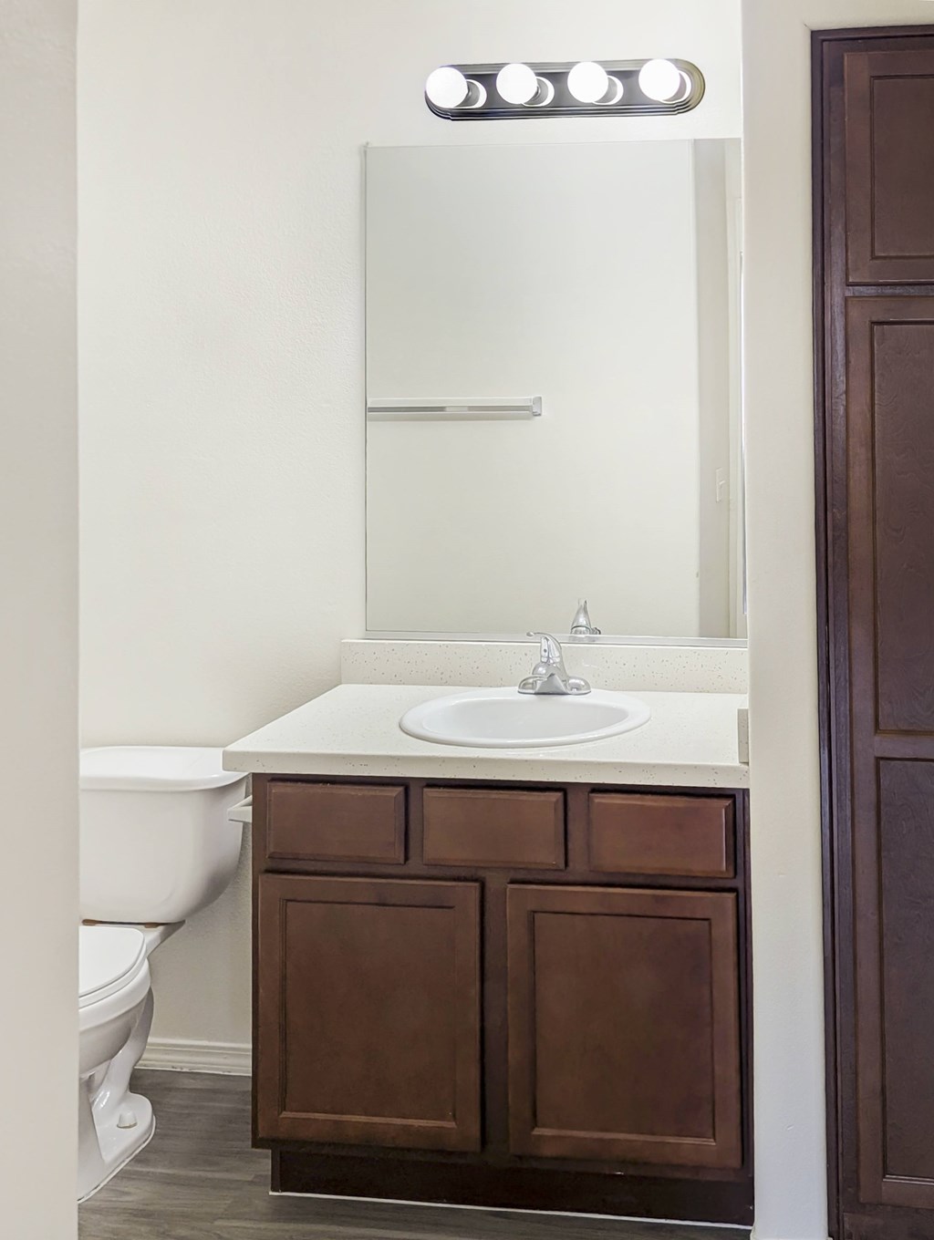 A white sink is on a brown cabinet under a mirror with lights.