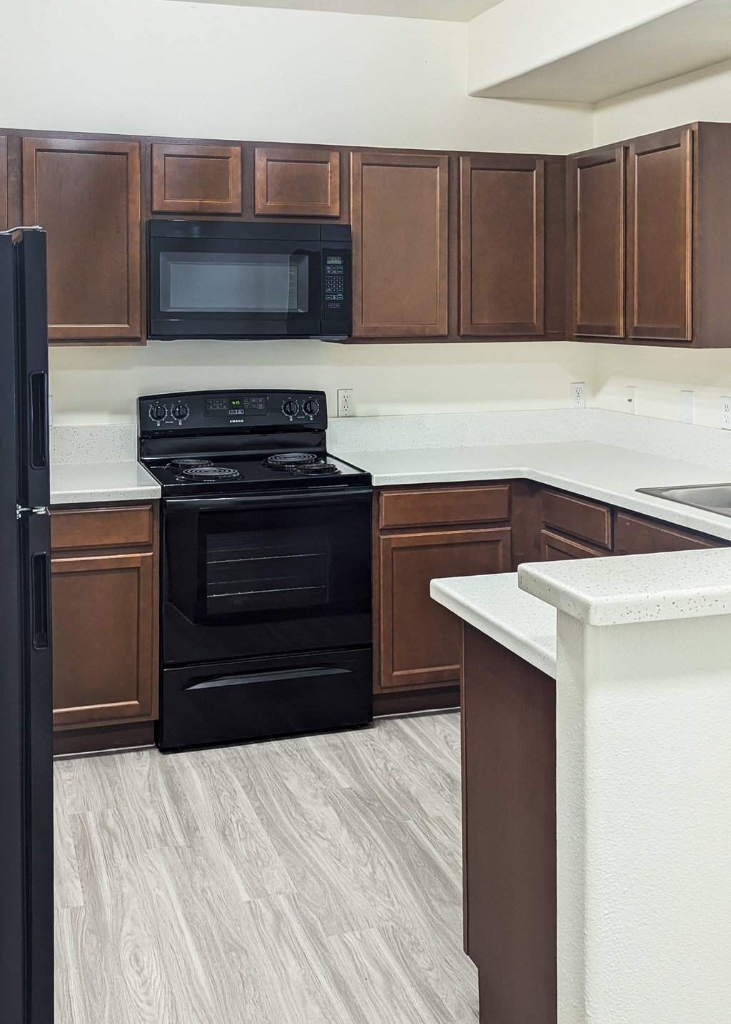 A black refrigerator stands next to a black stove in a kitchen with brown cabinets.