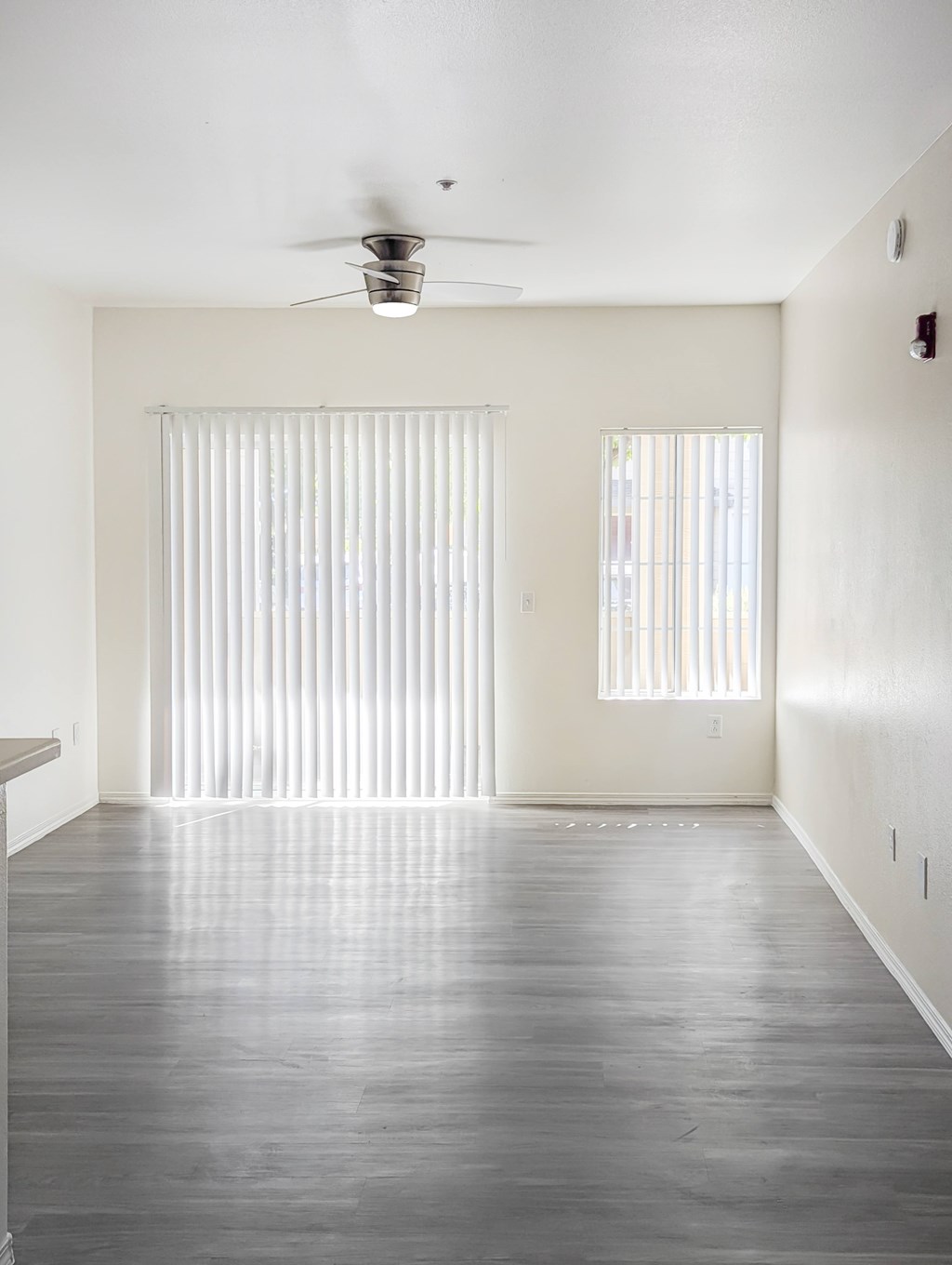 A room with a ceiling fan and two windows with blinds.