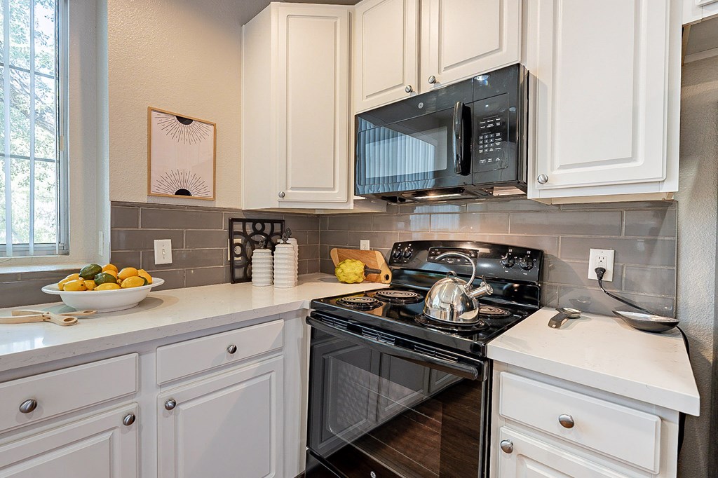 A black microwave is mounted above a black stove in a kitchen with white cabinets.at Palazzo Townhomes, Phoenix  