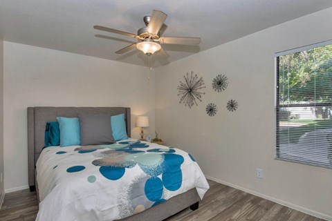 A bedroom with a bed, pillows, a ceiling fan, and a window with blinds at Reflections at Red Mountain Apartments, Arizona