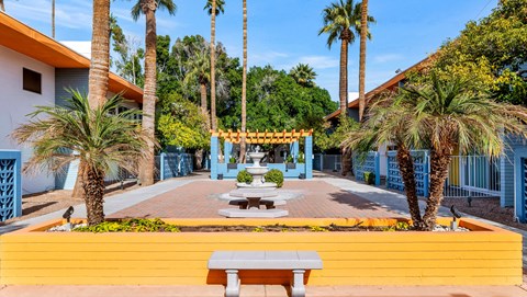 A bright yellow bench sits in front of a blue building with a palm tree at The Phoenix Apartments on 6th Avenue, Phoenix