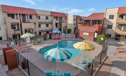 A pool surrounded by a fence and umbrellas in front of apartment buildings. at Urban WalkApartments on 6th Avenue, Phoenix, Arizona