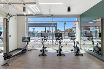 a gym with treadmills and exercise bikes in front of a large window at Melody on Main, Mesa, AZ