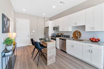 a kitchen with white cabinets and a wooden island with two black chairs at Melody on Main, Mesa, 85210