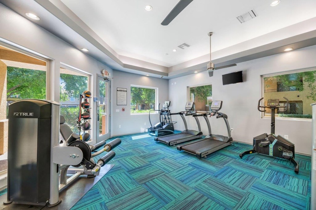 a gym with cardio equipment and windows in the corner of a room