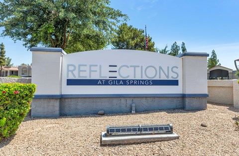 A sign that says "Reflections at Gila Springs" is in front of a tree.