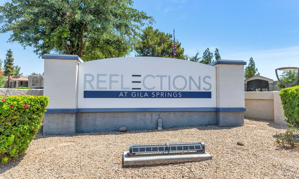 A sign that says "Reflections at Gila Springs" in front of some trees.
