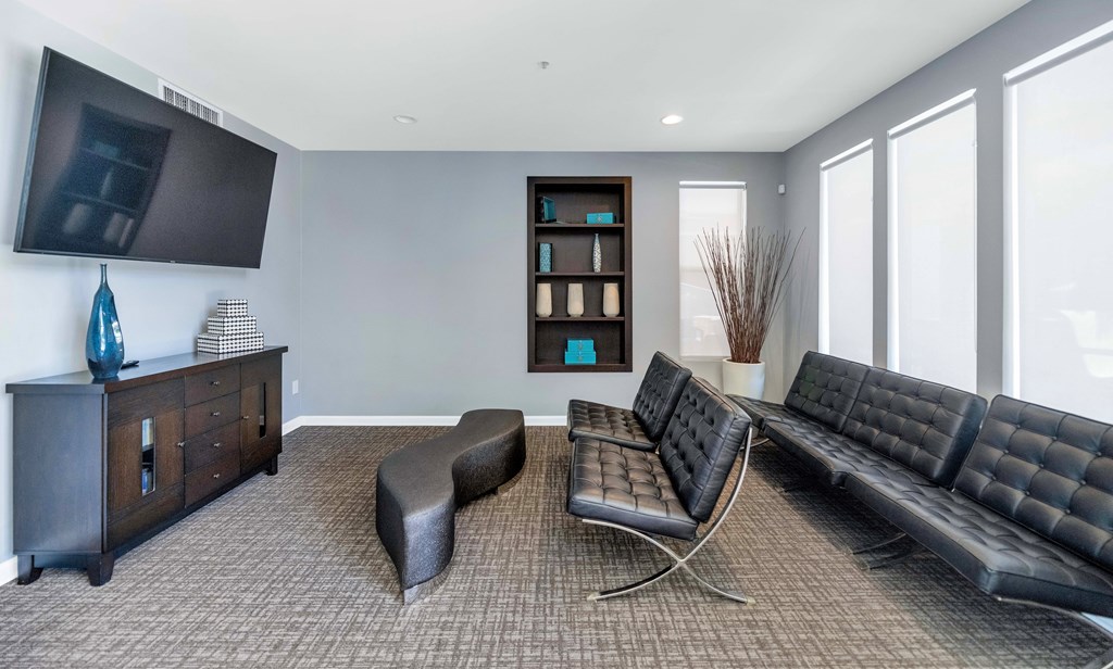 A living room with a black leather couch, a grey ottoman, and a wooden cabinet with a flat screen TV mounted above it.
