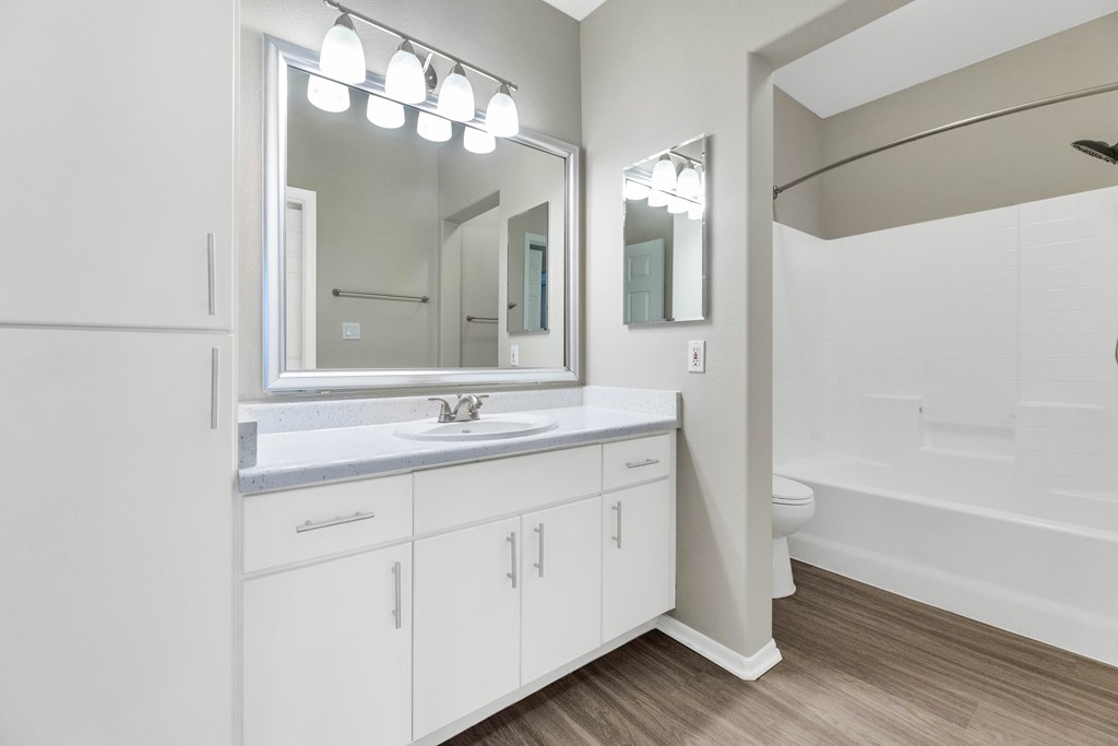 A white bathroom with a sink, mirror, and wooden floors.