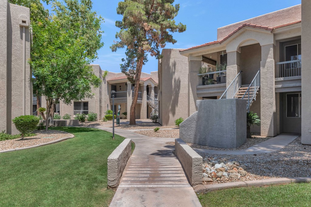 A concrete walkway leads to a building with a balcony.
