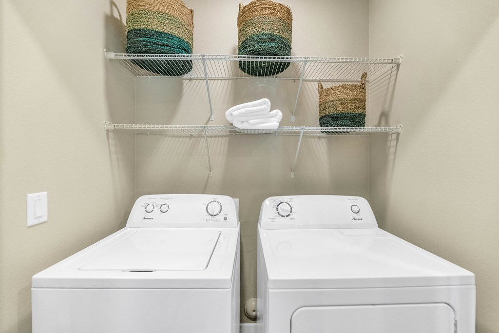 two white washers and dryers in a laundry room with shelves and baskets