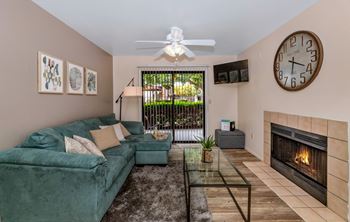 A living room with a green couch, a fireplace, and a ceiling fan at Reflections at Red Mountain Apartments, Mesa, Arizona