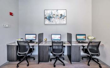 four desks with computers and chairs in an office with a painting on the wall