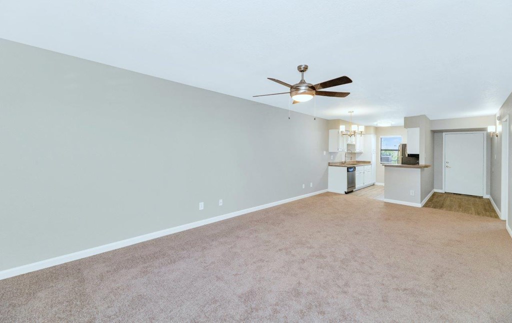 a living room with a ceiling fan and a kitchen in the background