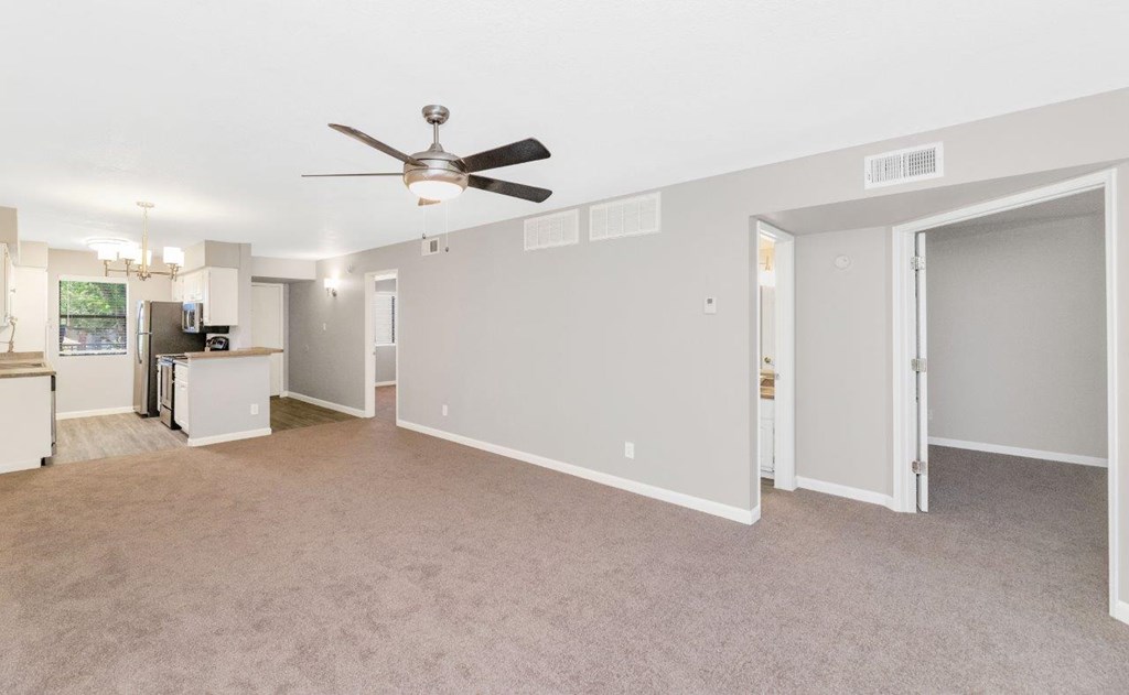a living room with a ceiling fan and a kitchen in the background