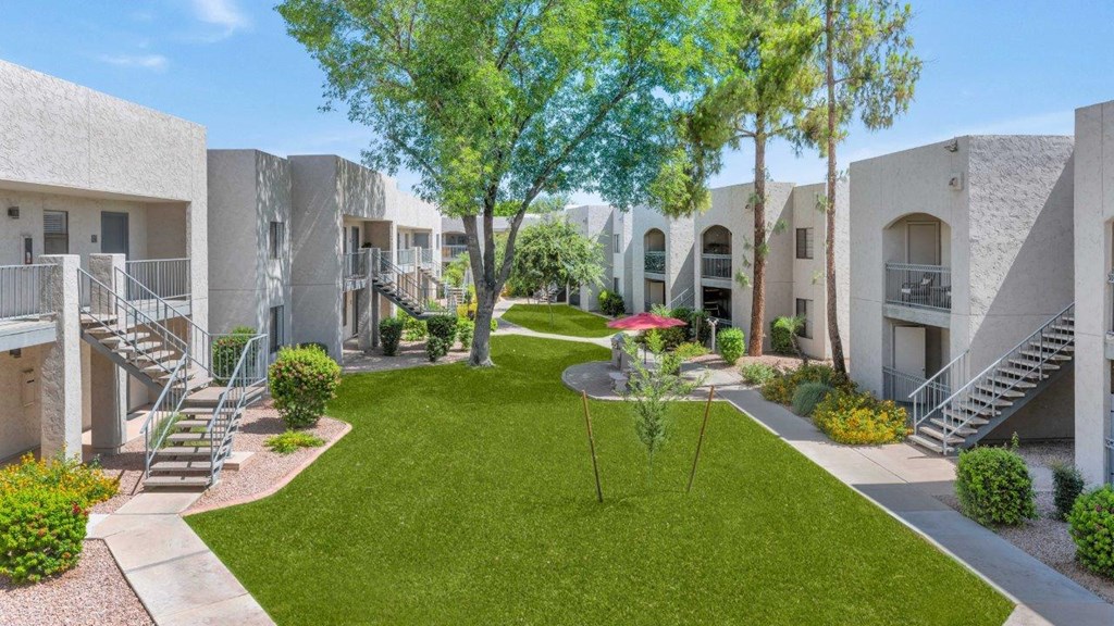 an exterior view of an apartment complex with a grassy area and trees