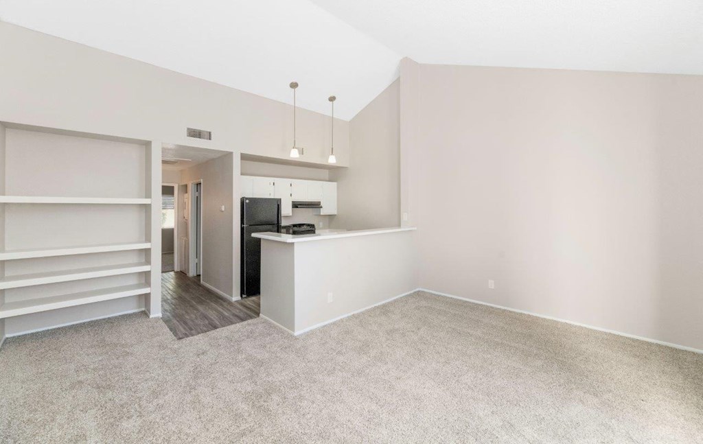 an empty living room with a kitchen in the background