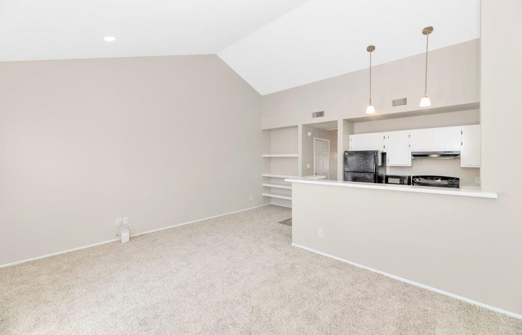 an empty living room with a kitchen in the background