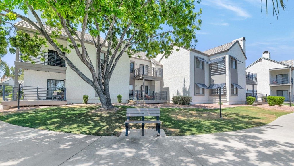 a park bench sits in the middle of a grassy area in front of some apartments