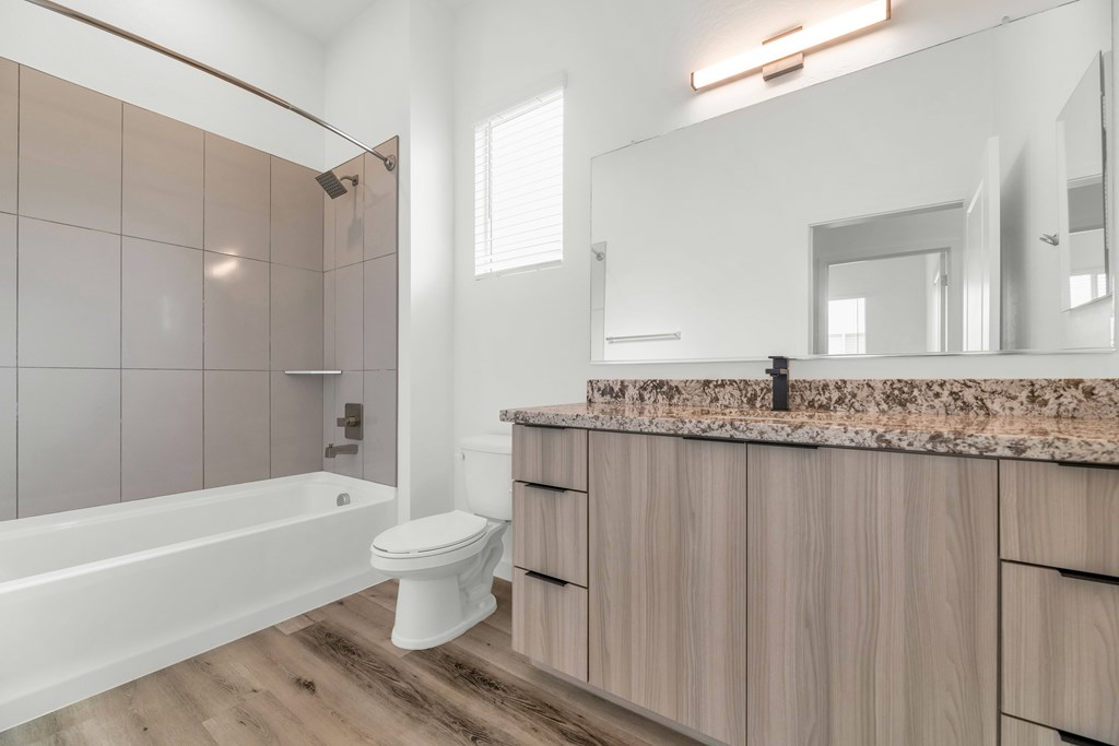 A white toilet sits in a modern bathroom with wooden cabinets and a marble countertop at Marketside Villas at Verrado, Buckeye, AZ