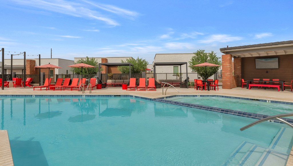 A large swimming pool with red lounge chairs and umbrellas at Marketside Villas at Verrado, Buckeye, AZ
