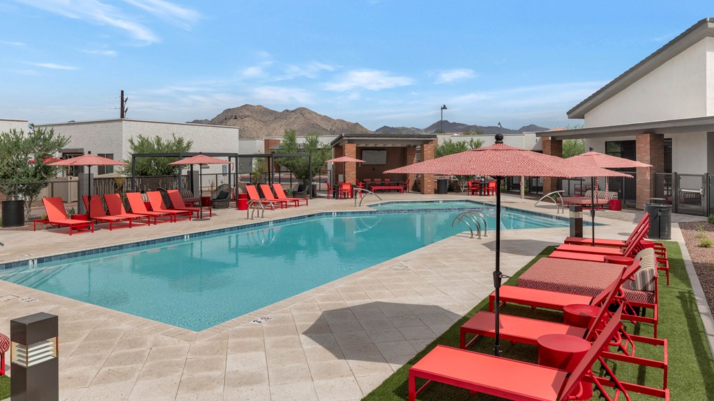 A pool surrounded by red chairs and umbrellas at Marketside Villas at Verrado, Buckeye, AZ
