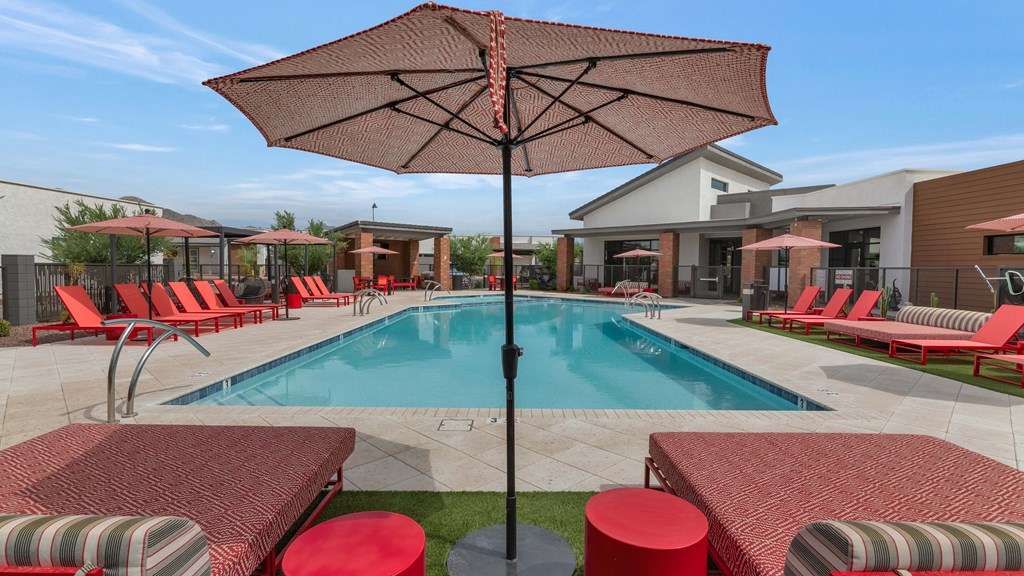 A pool area with red chairs and a red umbrella at Marketside Villas at Verrado, Buckeye, AZ
