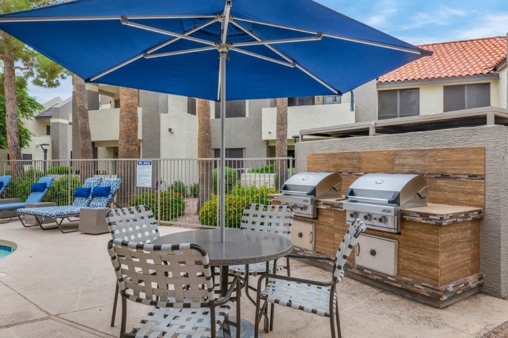 a patio with a grill and tables with chairs and umbrellas