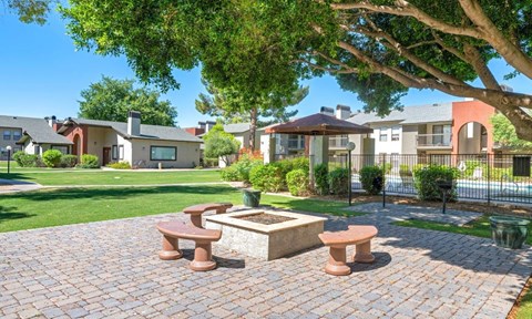 A brick patio with a fire pit and benches is surrounded by greenery and houses at Reflections at Red Mountain Apartments, Mesa, AZ, 85213