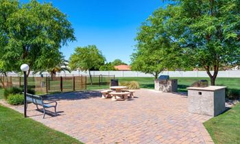 A park with a bench, picnic table, and a tree at Reflections at Red Mountain Apartments, Arizona