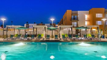 a swimming pool with chairs and umbrellas at night