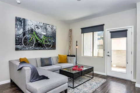 A living room with a grey couch, a coffee table, and a painting of a bicycle on the wall.