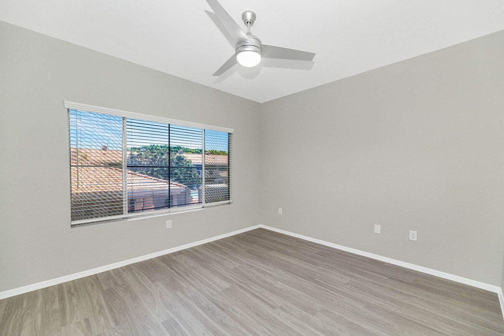 an empty living room with a large window and a ceiling fan