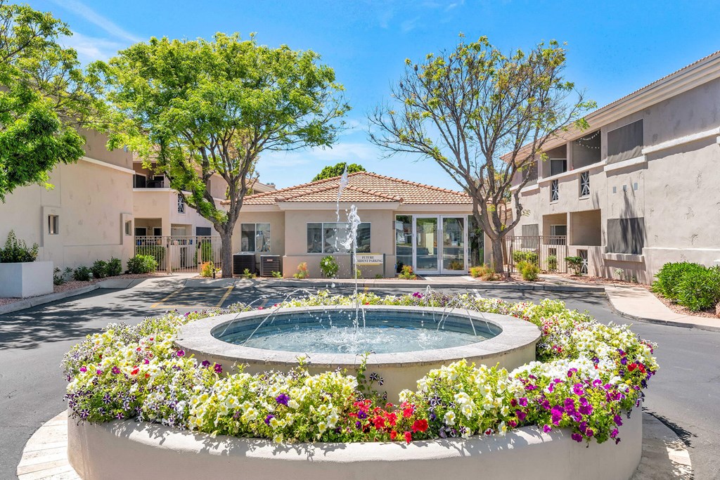 a fountain in front of an apartment building with flowers