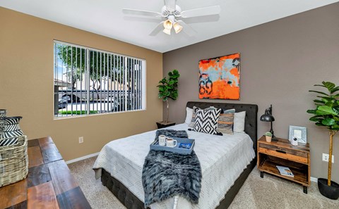 A bedroom with a large bed, a ceiling fan, and a window with blinds at Montage at Pecos Ranch Apartments, Arizona