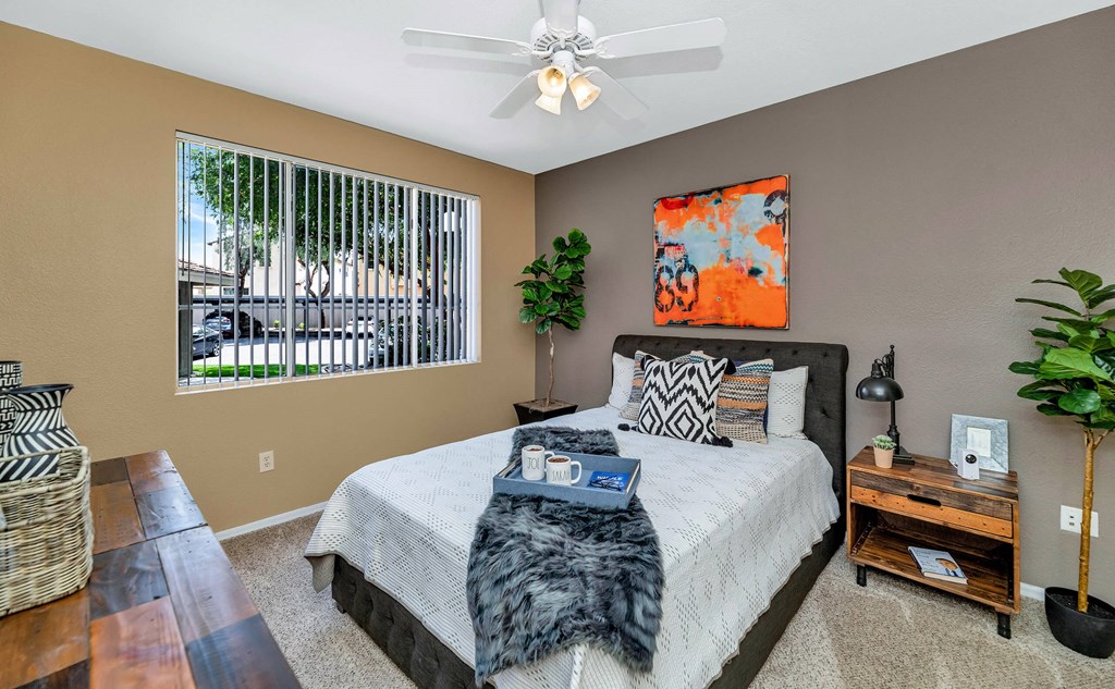A bedroom with a large bed, a ceiling fan, and a window with blinds. A bedroom with a large bed, a ceiling fan, and a window with blinds at Montage at Pecos Ranch Apartments, Arizona