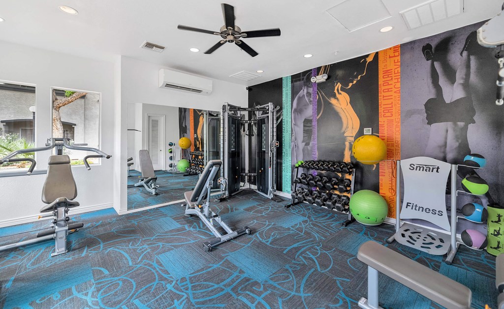 A gym with a variety of equipment including a bench, weights, and a squat rack at Montage at Pecos Ranch Apartments, Chandler
