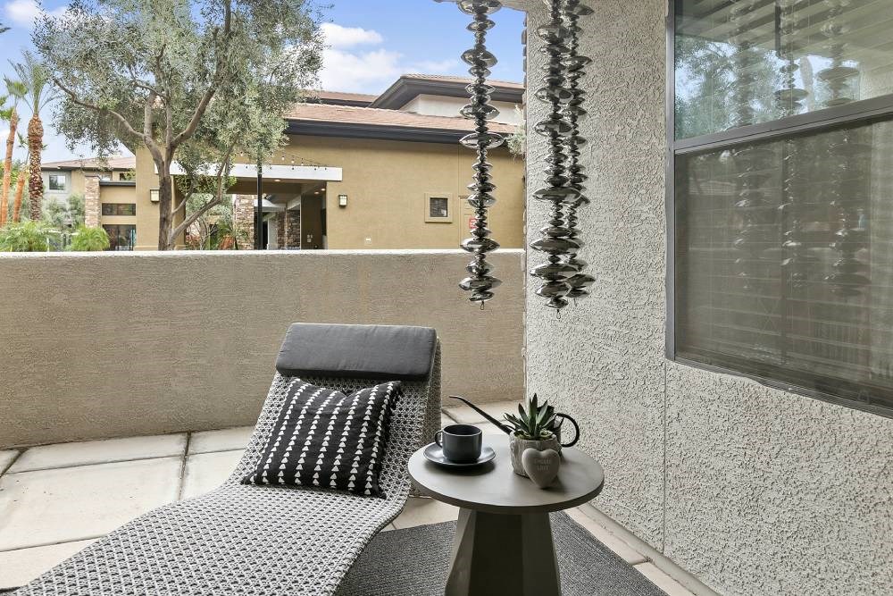A grey chair with a black cushion is on a patio with a table in front of a building. at The Laurel Apartments, Arizona