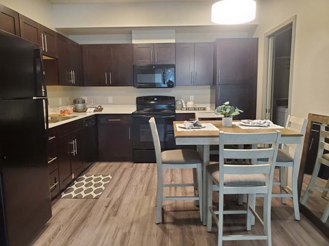 A kitchen with a black refrigerator and a dining table with chairs.