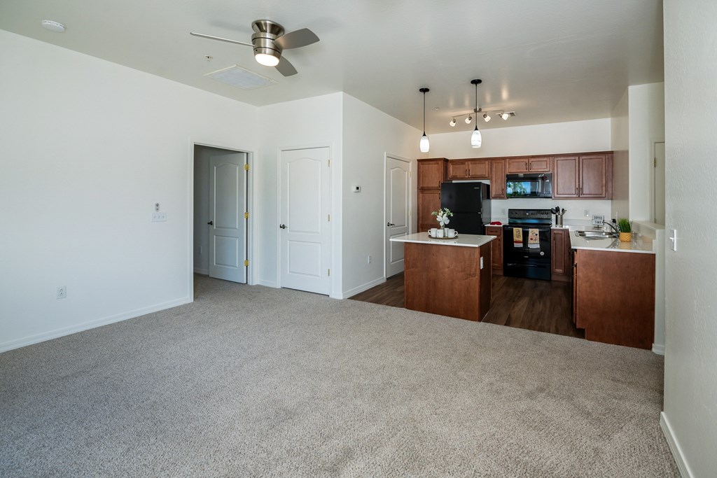 an empty living room with a kitchen and a ceiling fan