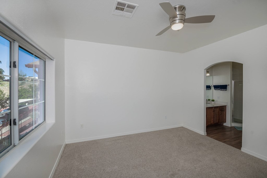 an empty living room with a large window and a ceiling fan