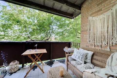 A balcony with a couch, table, and a view of trees.