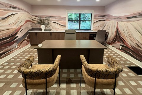 A room with a large table and chairs in front of a wall mural.