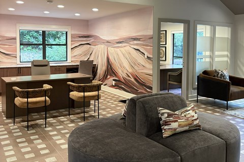 A living room with a grey sofa and a painting of a desert landscape on the wall.