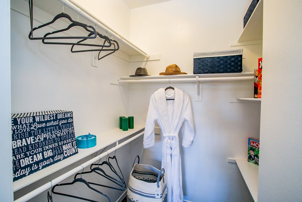 a walk in closet with a white robe and shoes and a shelf with hangers