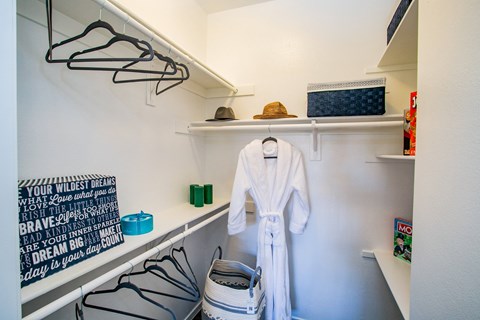 a walk in closet with a white robe and shoes and a shelf with hangers